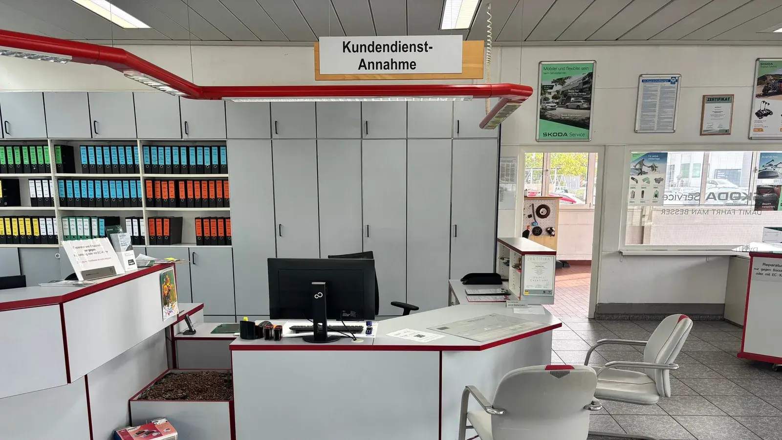 Arbeitsplatz im Service: Kundendienst-Annahme des Automobilsalon Bellemann in Wiesloch mit Tresen, Bildschirm, Ordnerregal und Stühlen für wartende Kunden