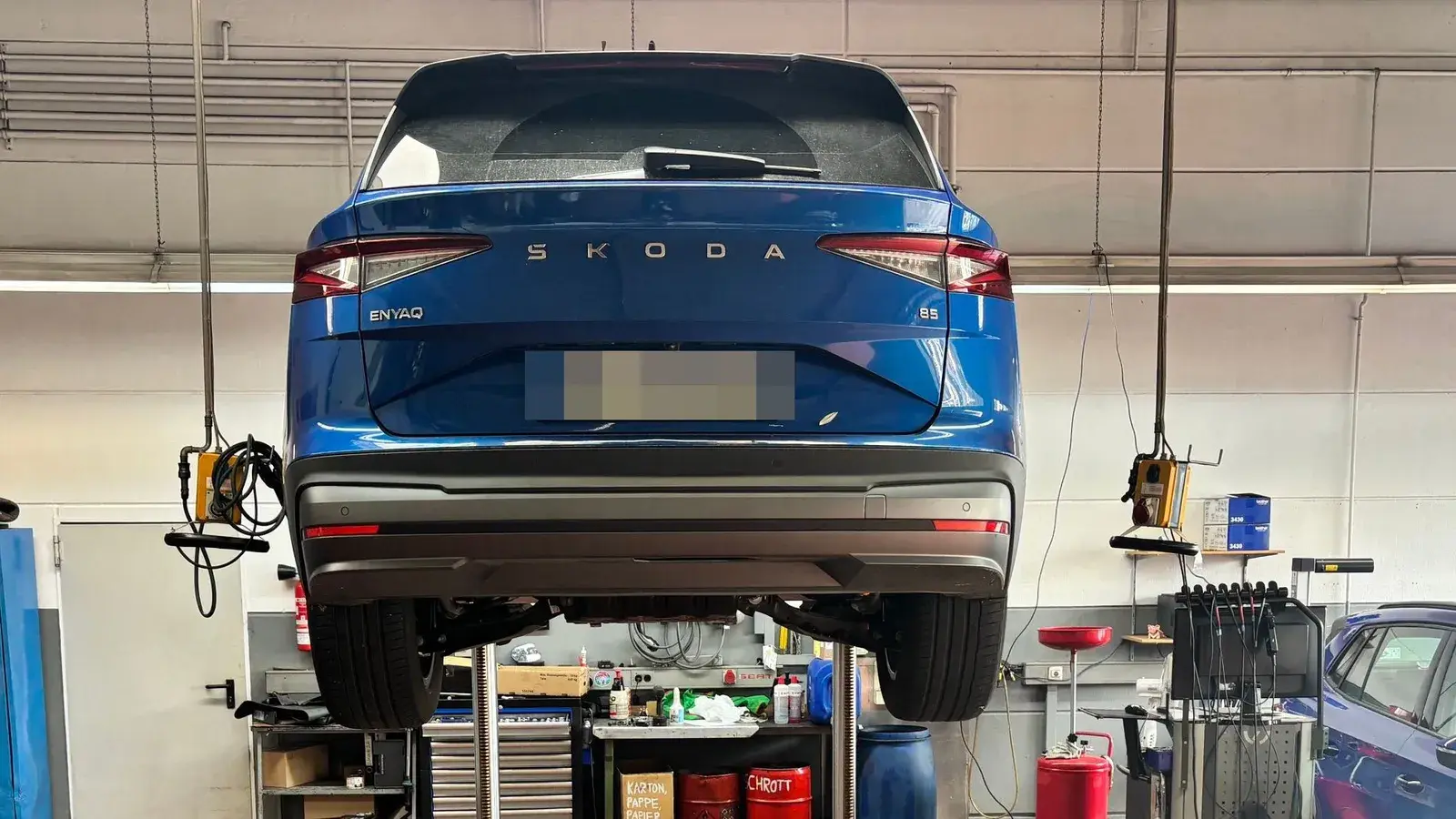 Arbeitsplatz in der Kfz-Werkstatt: ŠKODA Enyaq auf der Hebebühne beim Automobilsalon Bellemann in Wiesloch, darunter Werkzeugwagen und Auffangbehälter