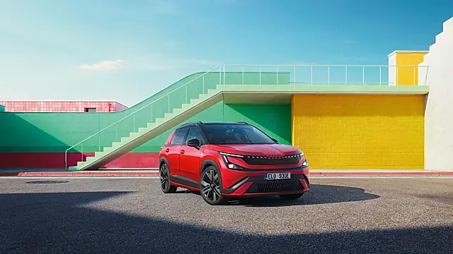Škoda Epiq Sportline in Rot mit schwarzem Dach: schräg von vorn mit leuchtendem Lichtband vor bunten Mauern