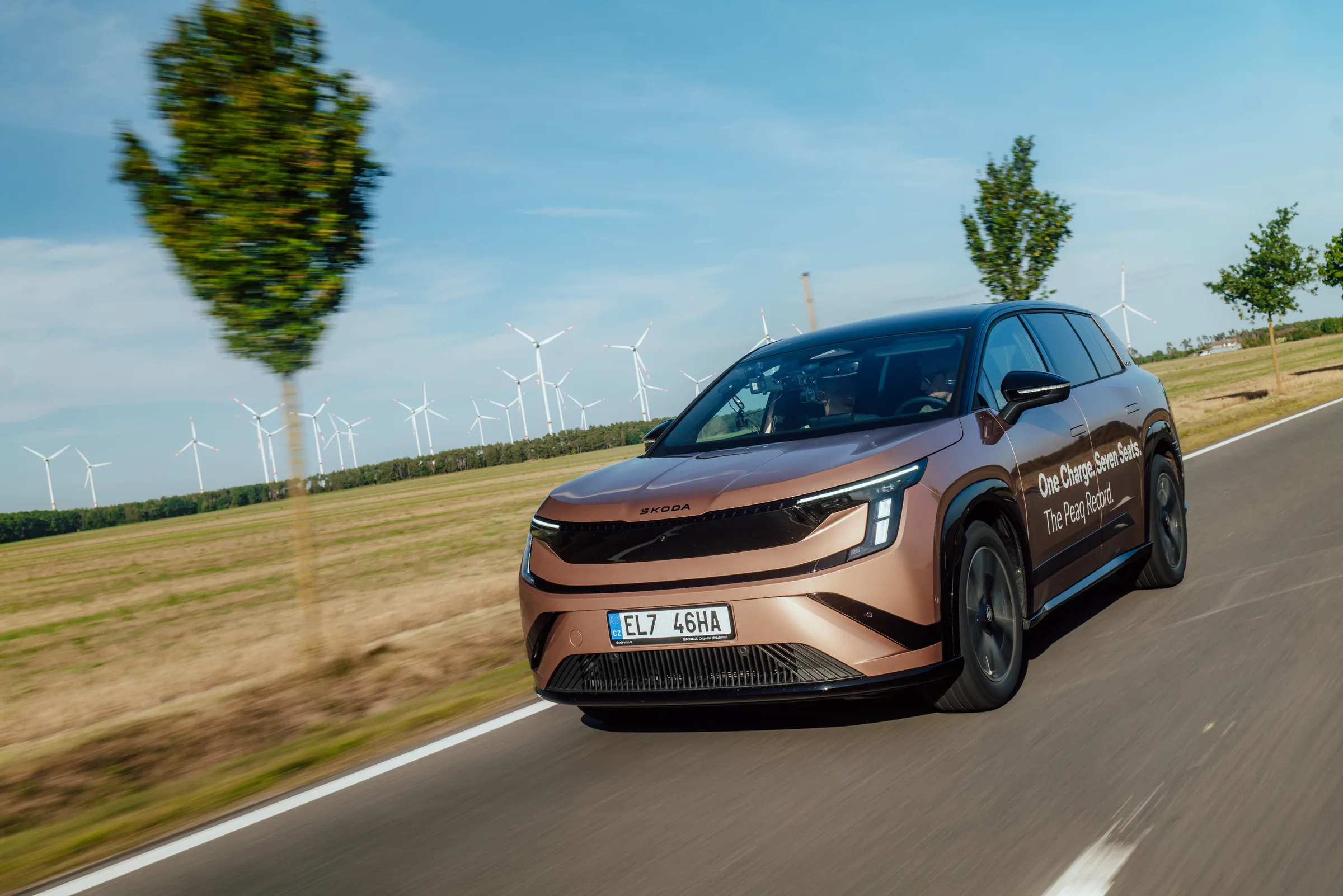 Škoda Peaq Reichweitenrekord: roségoldenes Rekordfahrzeug mit Türaufschrift auf einer Landstraße vor Windrädern